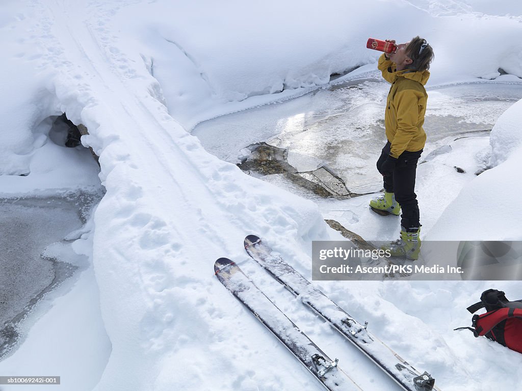 Man standing in snow drinking water from bottle, side view