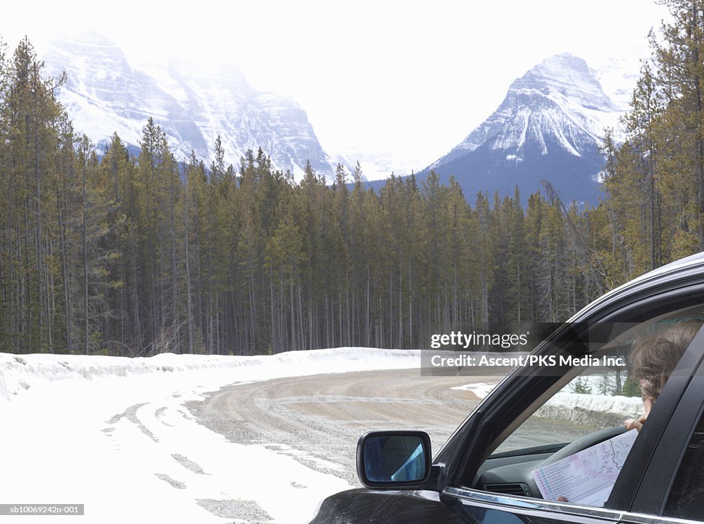 Man sitting in car holding map on snowy road