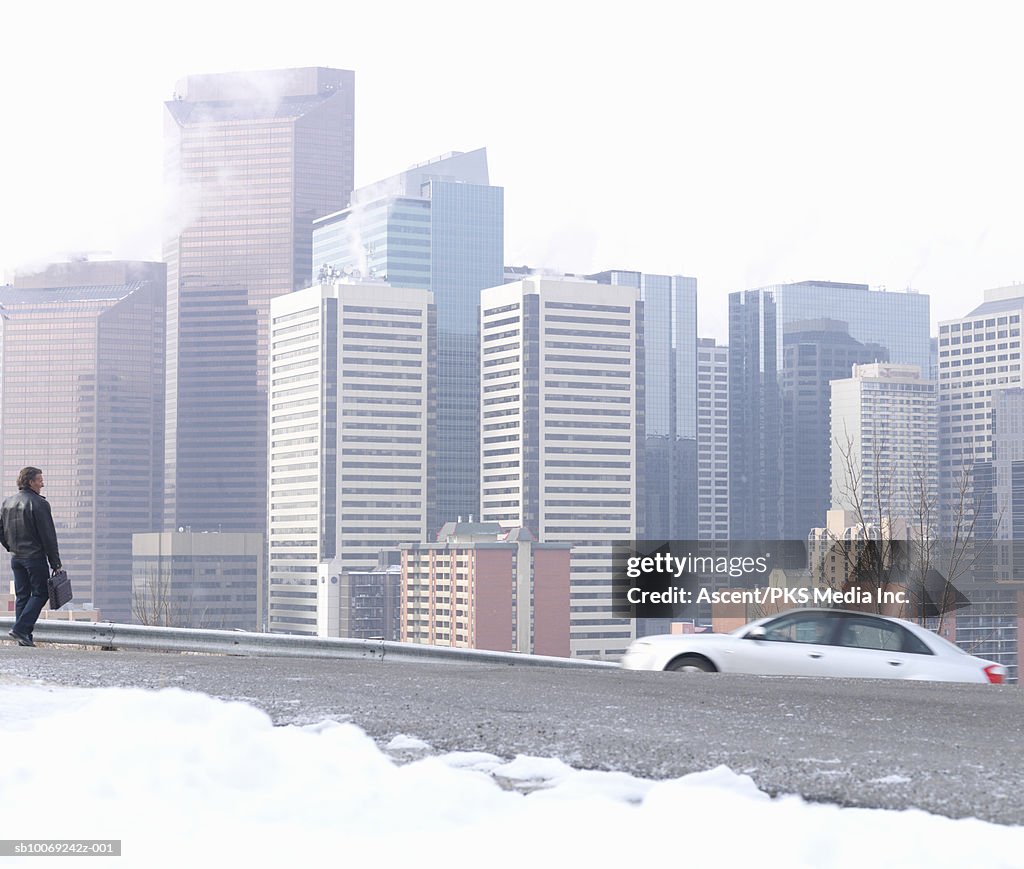 Man walking on snowy street, city skyline in background