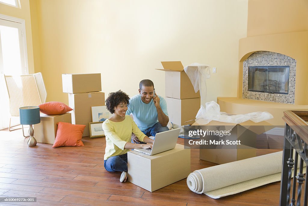 Couple using laptop between boxes in unfurnished room