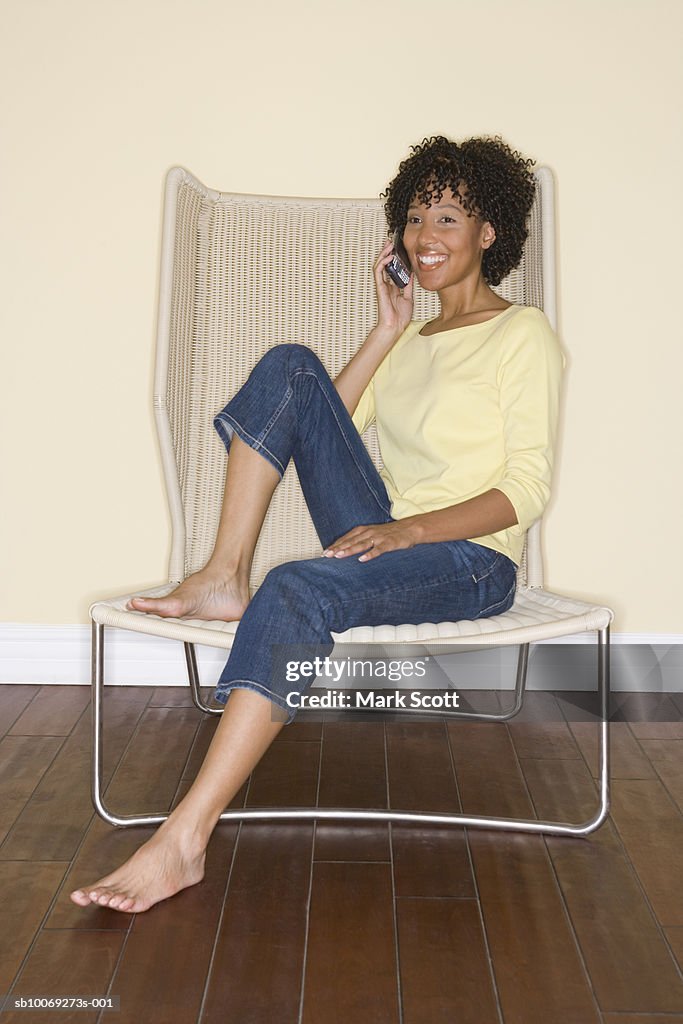 Woman using mobile phone sitting on chair, portrait
