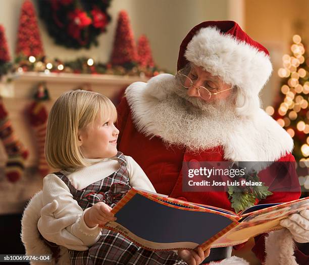 girl (4-5) sitting on santa's lap with book, smiling, close-up - santa close up stock-fotos und bilder