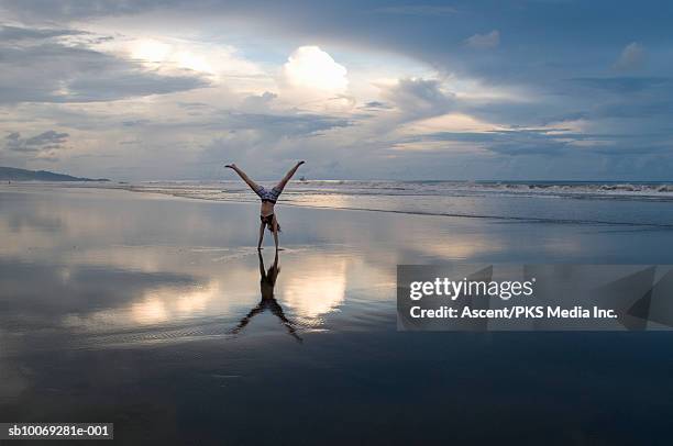 woman performing handstand on beach at sunset - handstand beach photos et images de collection