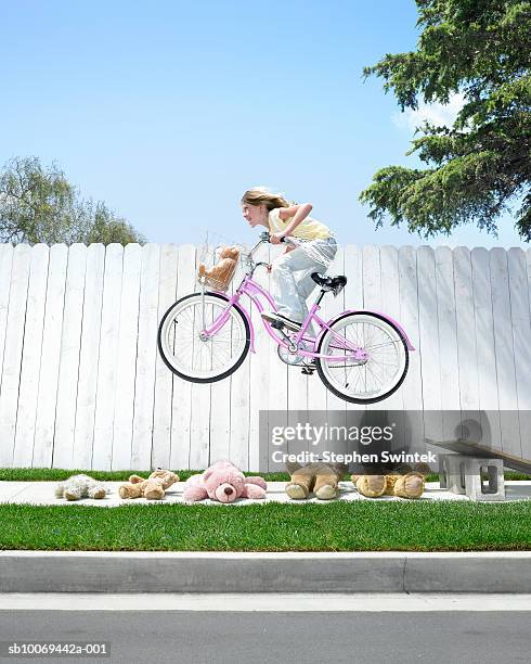 girl (8-9) jumping off ramp on bike above teddy bears - irreverent stock-fotos und bilder