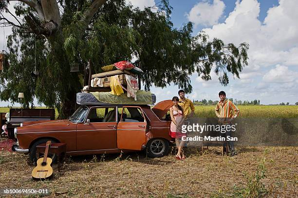 three people with house furniture on car roof standing in field, portrait - car roof stock pictures, royalty-free photos & images