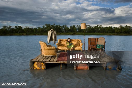 Young woman reading book on sofa on wooden raft