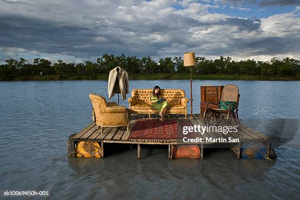 young woman reading book on sofa on wooden raft - moving sofa stock pictures, royalty-free photos & images