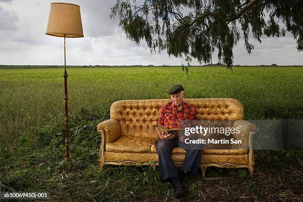 senior man reading book on sofa in field - mann lässig gras sitzen stock-fotos und bilder