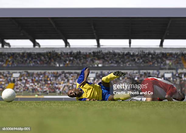 two male soccer players lying down after tackle in stadium - soccer injury stock pictures, royalty-free photos & images