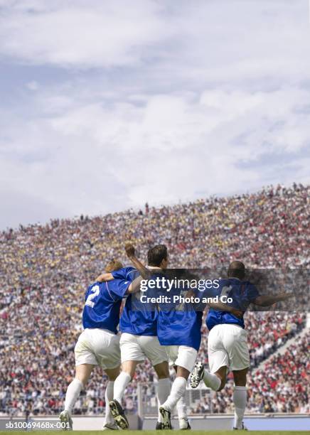 four male soccer players celebrating in stadium, rear view - joueur de football photos et images de collection