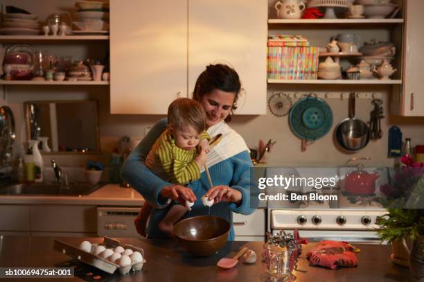 mother carrying baby boy (12-17 months) breaking eggs into bowl - busy kitchen stock pictures, royalty-free photos & images