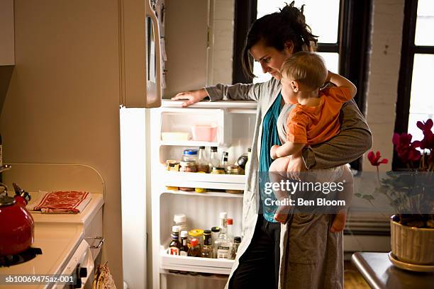 mother carrying son (12-17 months) looking through refrigerator, side view - fridge stock-fotos und bilder