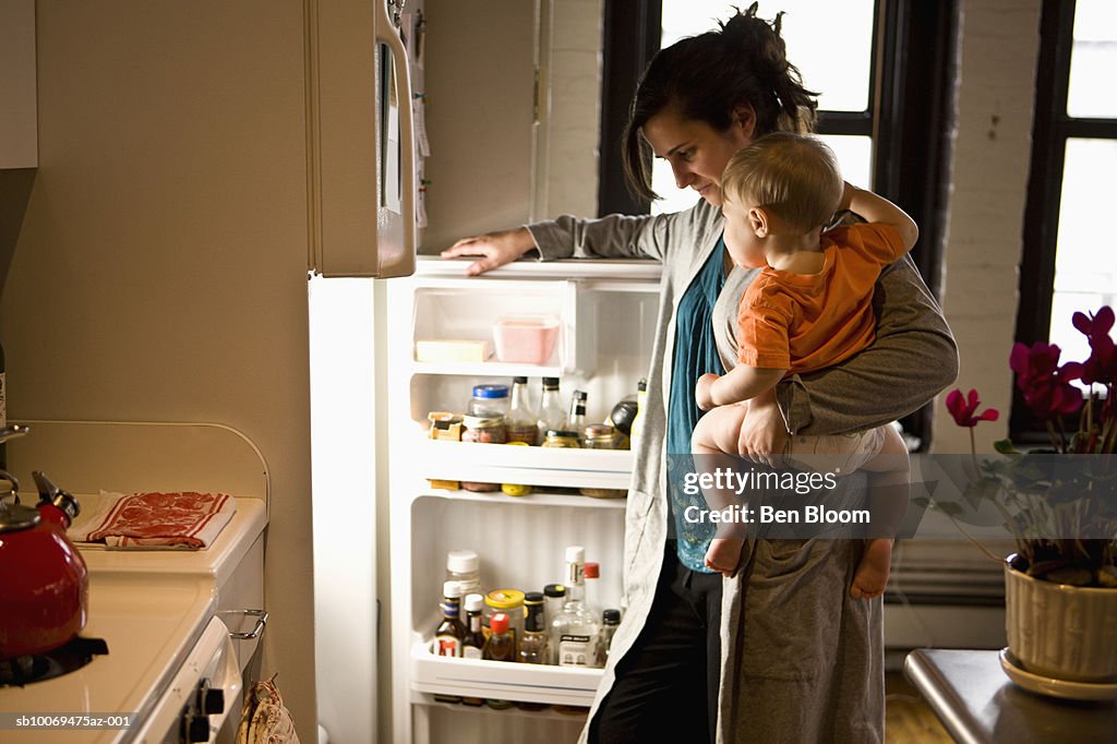 Mother carrying son (12-17 months) looking through refrigerator, side view