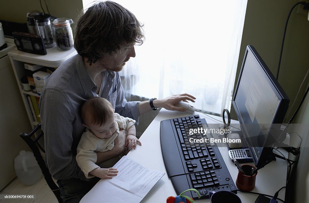 Father with baby boy (6-11 months) at table using computer, high angle view