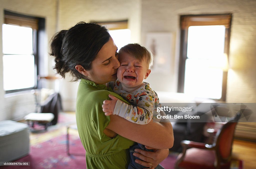 Mother holding and kissing crying baby boy (12-17 months) (focus on foreground)