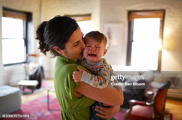mother holding and kissing crying baby boy (12-17 months) (focus on foreground) - baby standing stock pictures, royalty-free photos & images