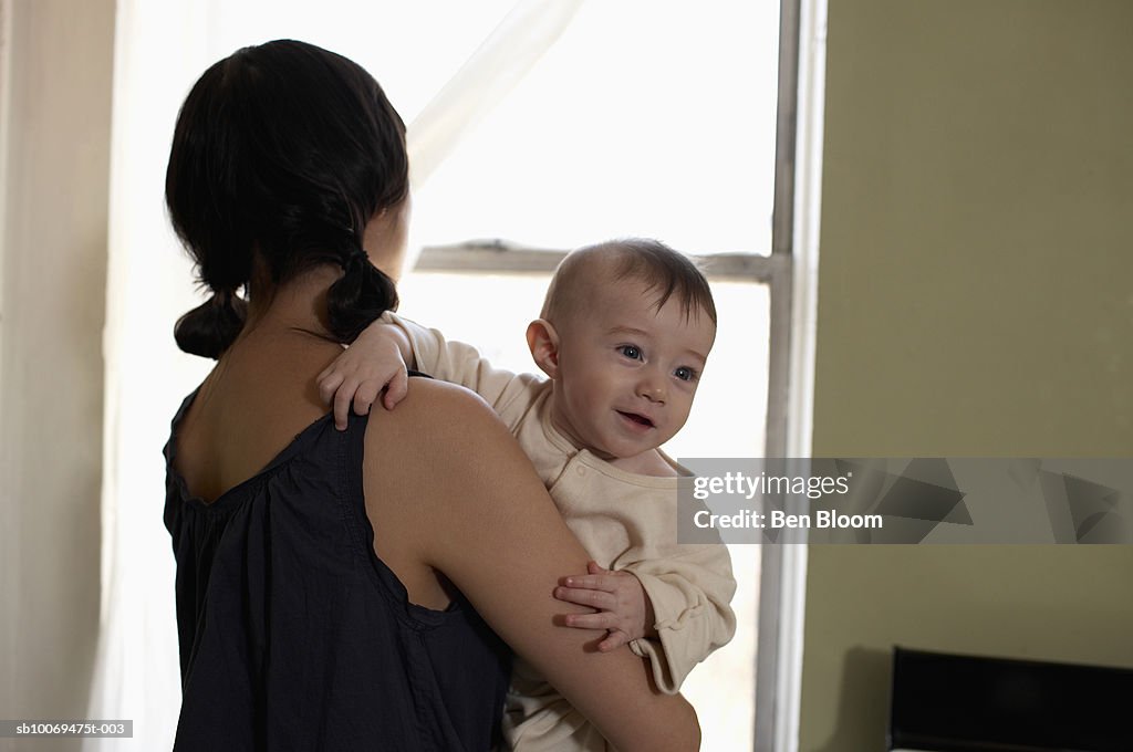 Mother holding son (6-11 months) looking out window