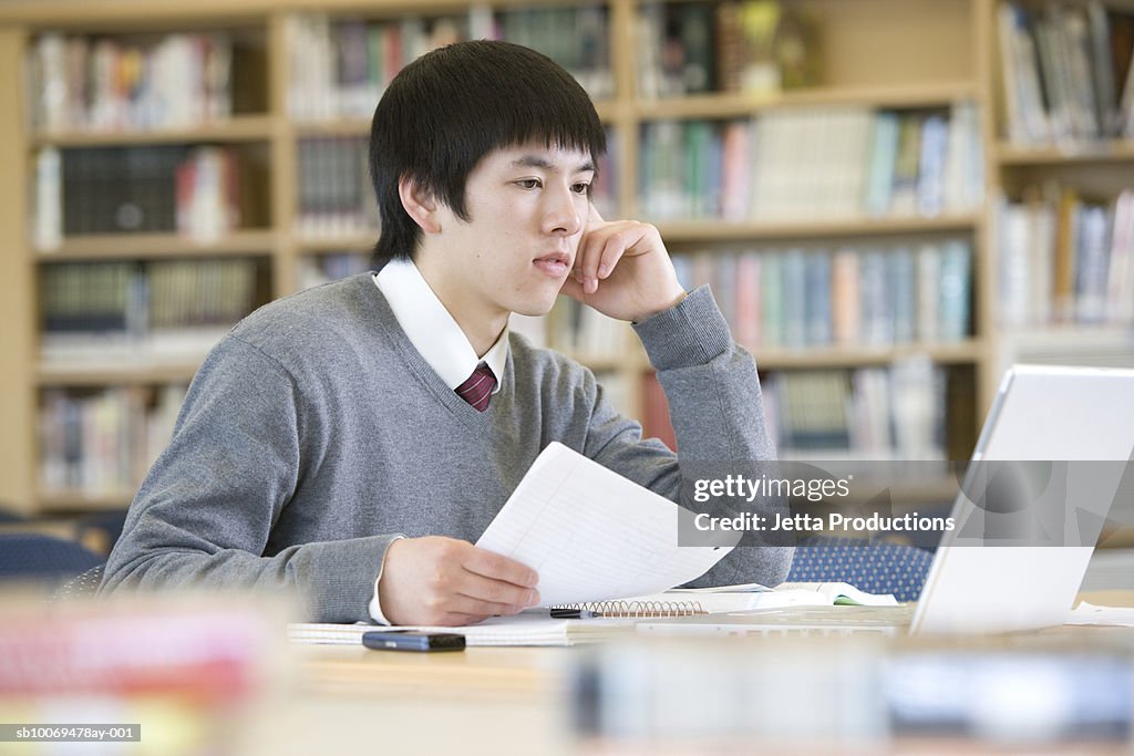 School boy (16-17) using laptop, working in library