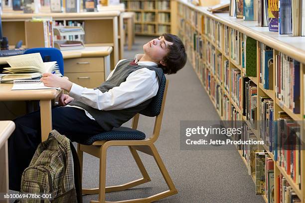 school boy (16-17) sleeping at desk in library - sleeping boys stockfoto's en -beelden