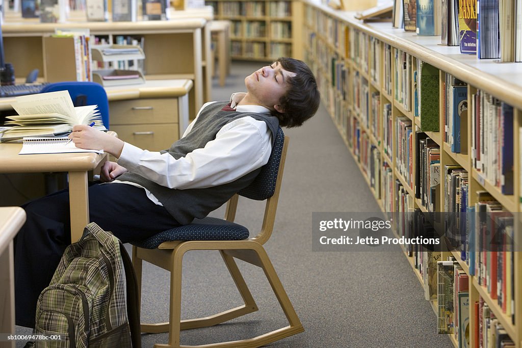 School boy (16-17) sleeping at desk in library