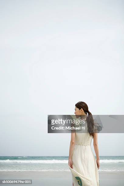 young woman standing on beach, rear view - encuadre de tres cuartos fotografías e imágenes de stock