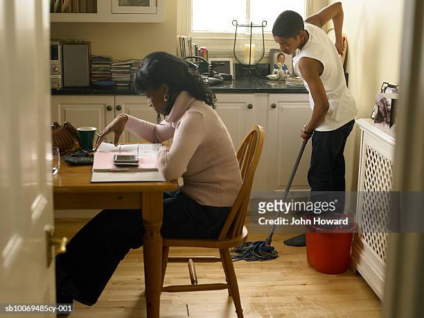 boy (12-13) mopping kitchen floor behind mother counting bills - kitchen mop stock pictures, royalty-free photos & images