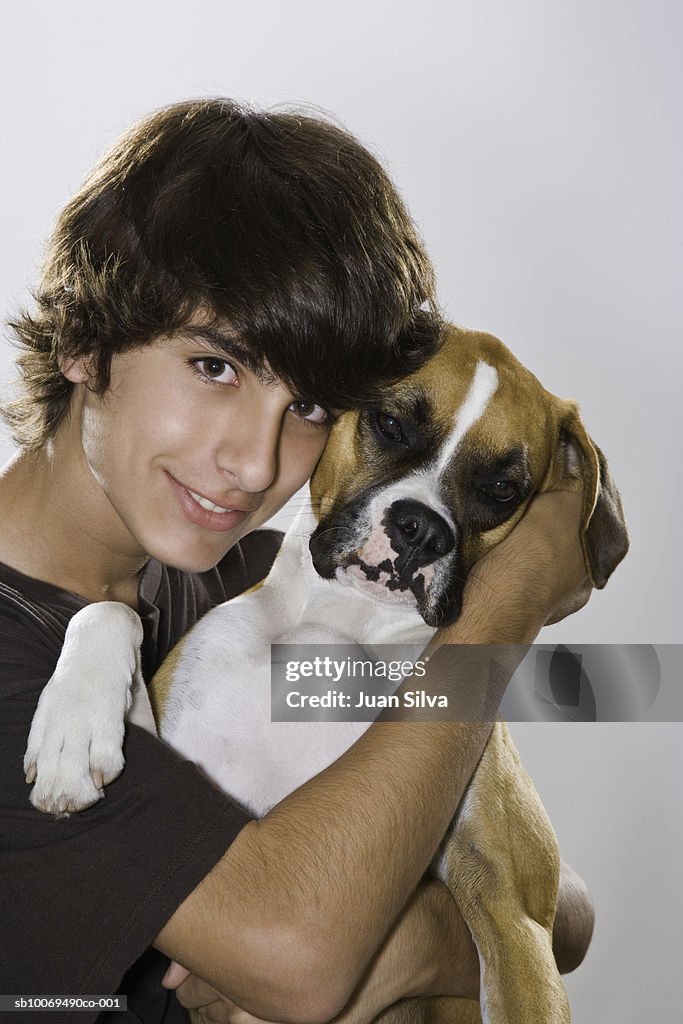 Boy (14-15) hugging boxer dog, studio portrait