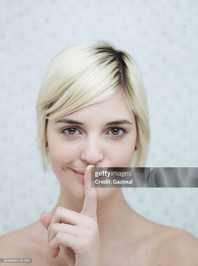 Young woman with finger on lips, smiling, portrait