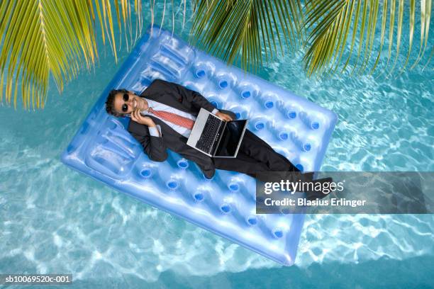 businessman using laptop and mobile phone, floating on airbed in pool - fato completo imagens e fotografias de stock