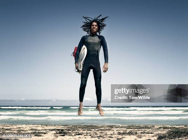 south africa, cape town, muizenburg, portrait of surfer with board, mid air - surfer wetsuit stock pictures, royalty-free photos & images
