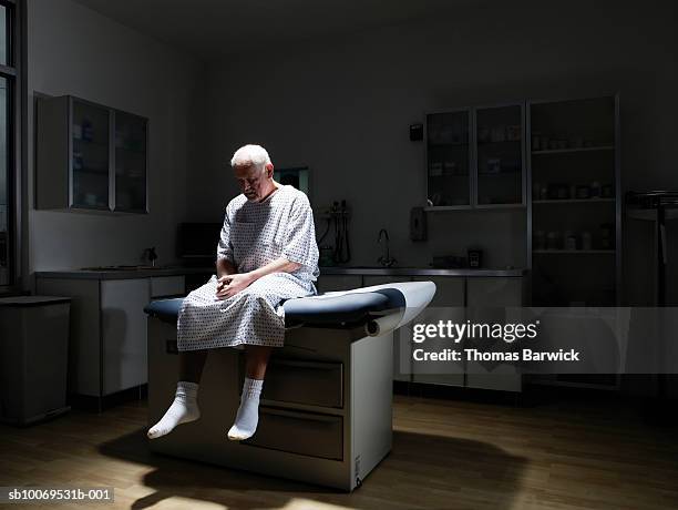 senior man sitting on examination table, looking down - kabinet dokter stockfoto's en -beelden
