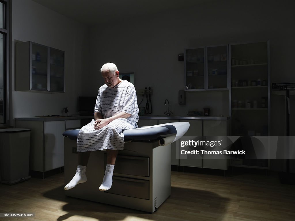 Senior man sitting on examination table, looking down