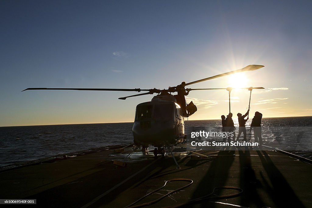 Silhouette of people cleaning helicopter at dusk