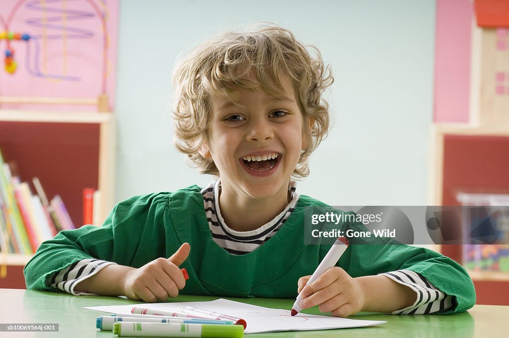 Boy (4-5) drawing picture at desk in classroom, portrait