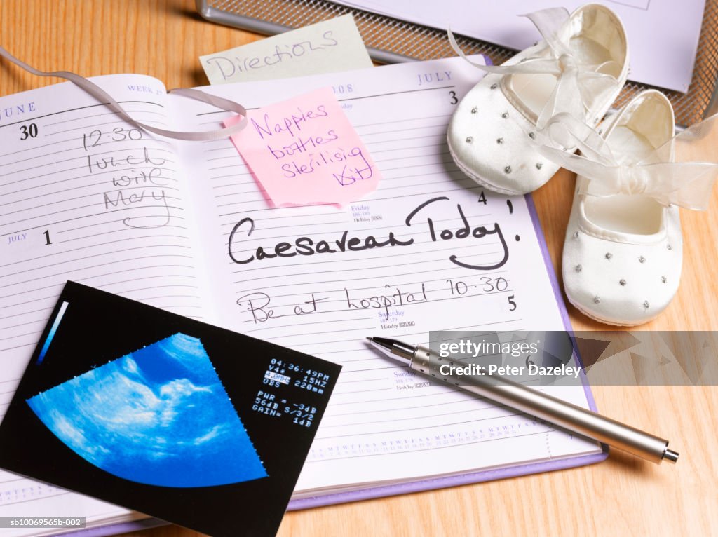 Diary and pen on desk with baby booties, high angle view