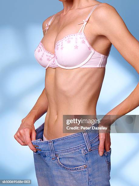 young woman pulling on waist of jeans, close-up - bony stock-fotos und bilder