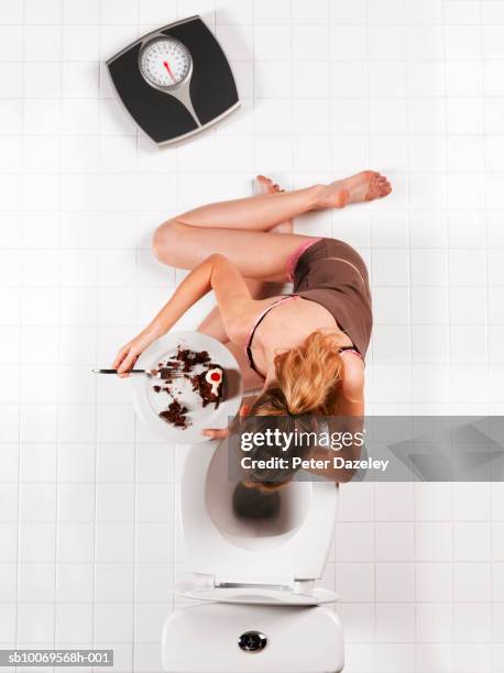 young woman with chocolate cake vomiting into toilet bowl, directly above - bulimie stock-fotos und bilder