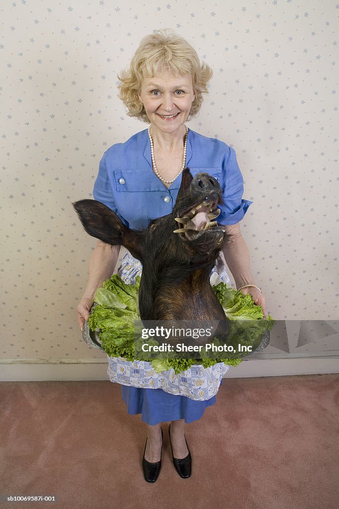 Senior woman holding wild boars head, portrait, high angle view