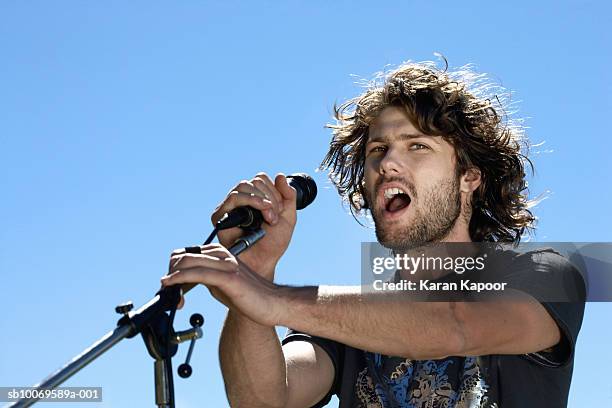 young man singing into microphone, view against blue sky - rock singers stock pictures, royalty-free photos & images