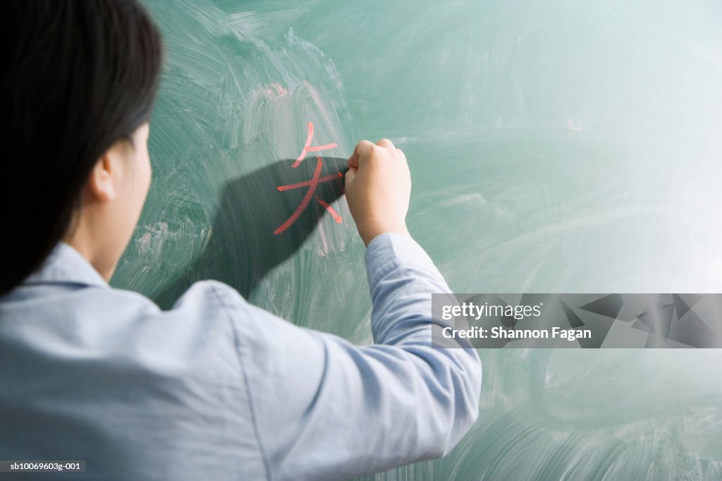 Female teacher writing on blackboard, rear view