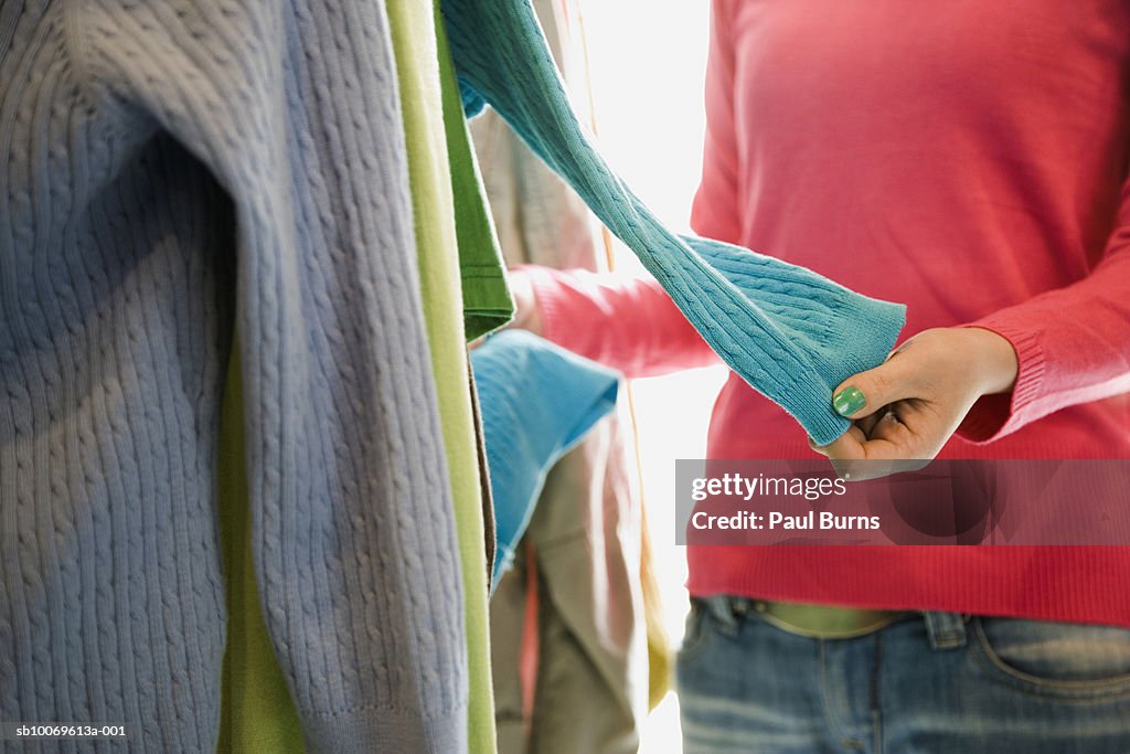 Young woman choosing sweater in shop, mid section