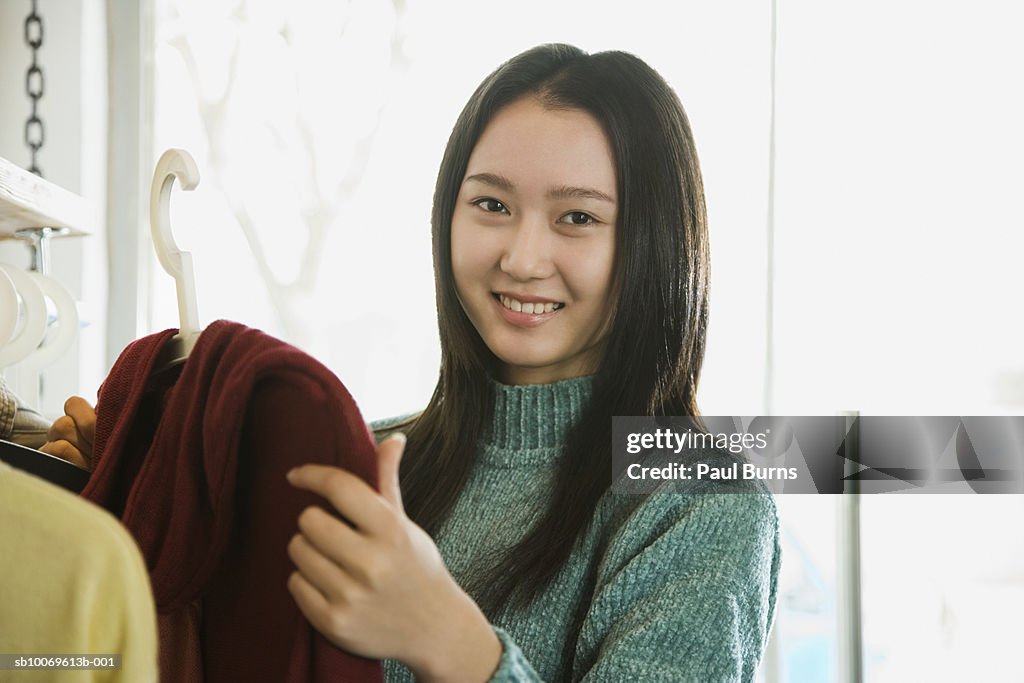 Young woman choosing sweater in shop, smiling, portrait