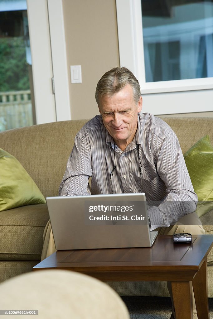 Mature man sitting in living room with laptop