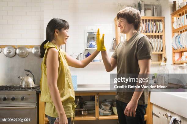 couple wearing rubber gloves touching hands in kitchen - bridging the gap stock pictures, royalty-free photos & images