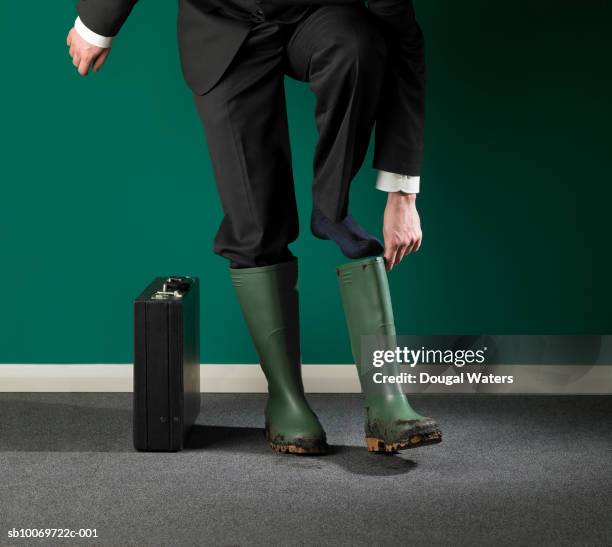 businessman putting on galoshes, low section - botas de agua fotografías e imágenes de stock