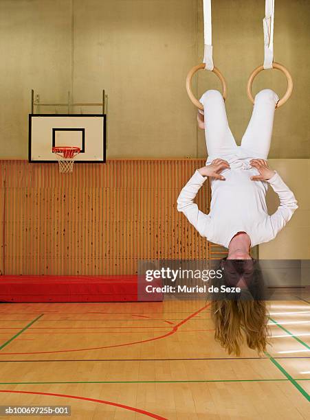 portrait of girl (8-9) hanging from rings in school gym - 逆さ ストックフォトと画像