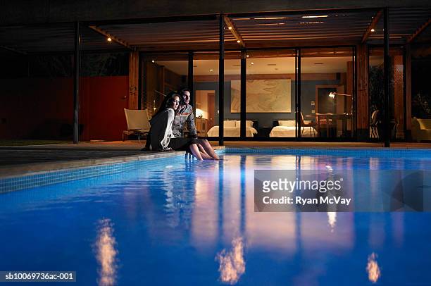 young couple sitting at edge of pool at night - couple lit stock pictures, royalty-free photos & images