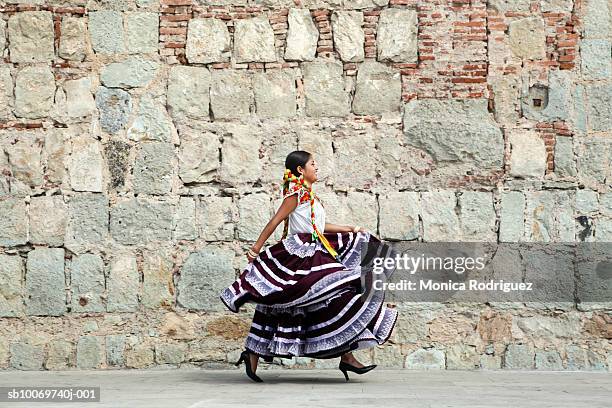 mexico, oaxaca, istmo, young woman in traditional dress walking by stone wall - oaxaca foto e immagini stock