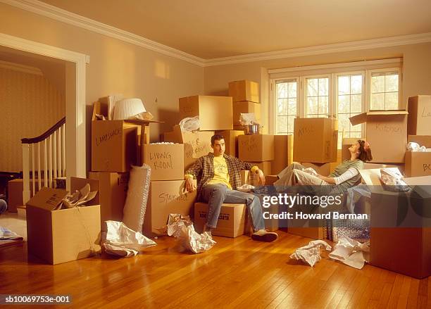 couple sitting with stack of packing boxes in room - trasloco casa foto e immagini stock