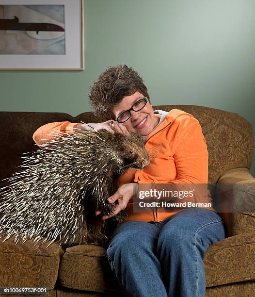 woman sitting on sofa petting porcupine, smiling - istrice foto e immagini stock